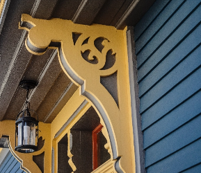 Decorative exterior wood bracket painted in warm yellow against blue siding, highlighting contrasting exterior paint colours