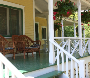 Covered front porch with painted green floor, white railing, and wicker seating, illustrating porch and floor paint colour options